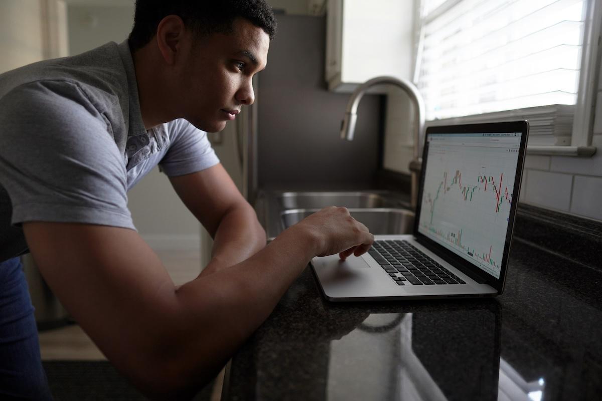 Un hombre joven analizando el mercado de acciones en su laptop para mejor entender cómo ganar ganar con acciones.